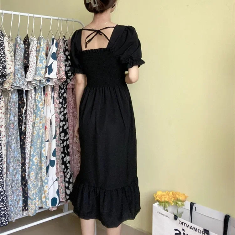 Black chiffon A-line dress with elastic waist, short puff sleeves and back tie, displayed with patterned dresses on rack