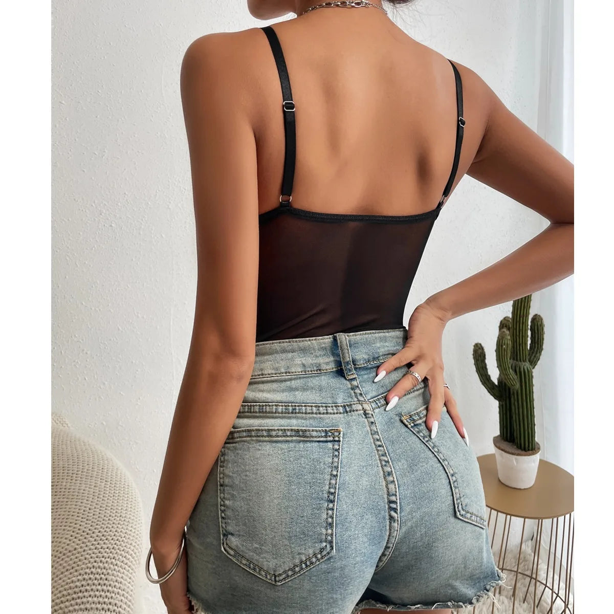 Black lace bodysuit for women, back view with adjustable straps; paired with blue denim shorts